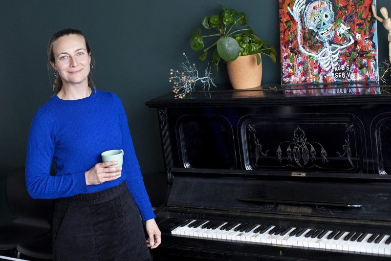 Kvinna med kaffekopp i ena handen står vid ett piano